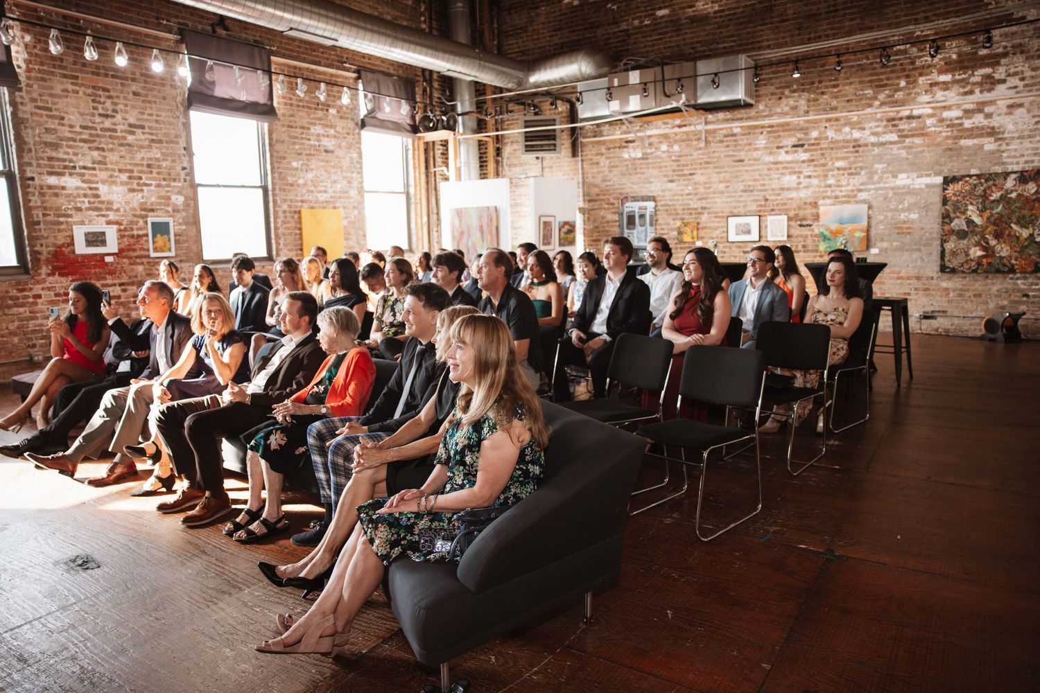 Wedding guests seated in a bright rustic brick wall art gallery ceremony space.