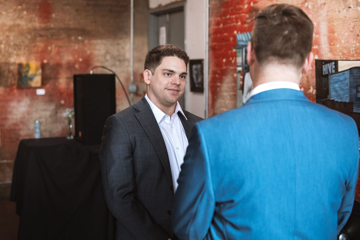 Two men in suits having a conversation at an indoor wedding reception venue.