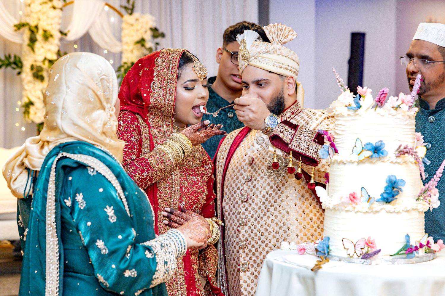 Bride and groom in traditional South Asian wedding attire feeding each other cake.