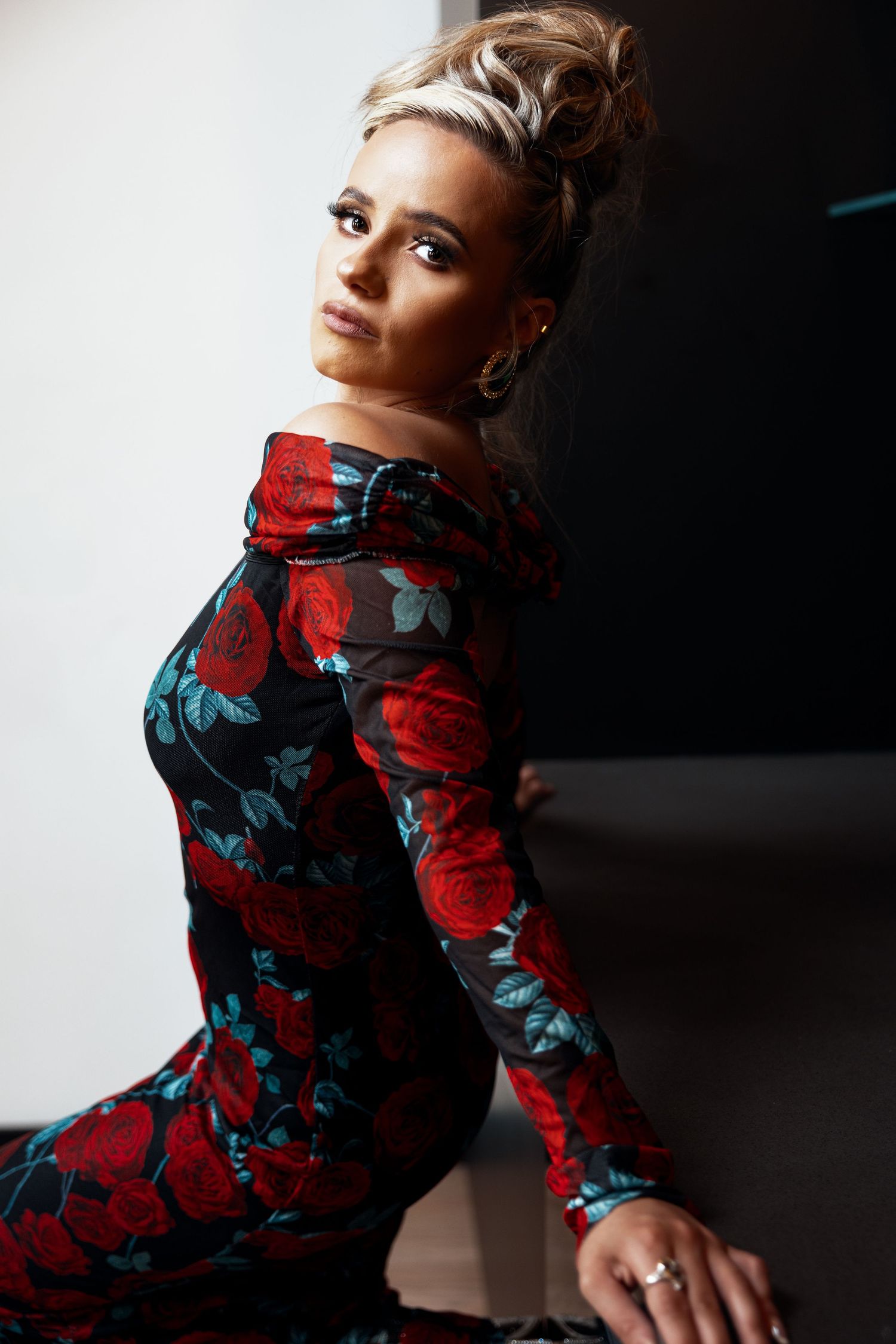Woman in floral red rose off-shoulder long sleeve dress posing elegantly with updo hairstyle.