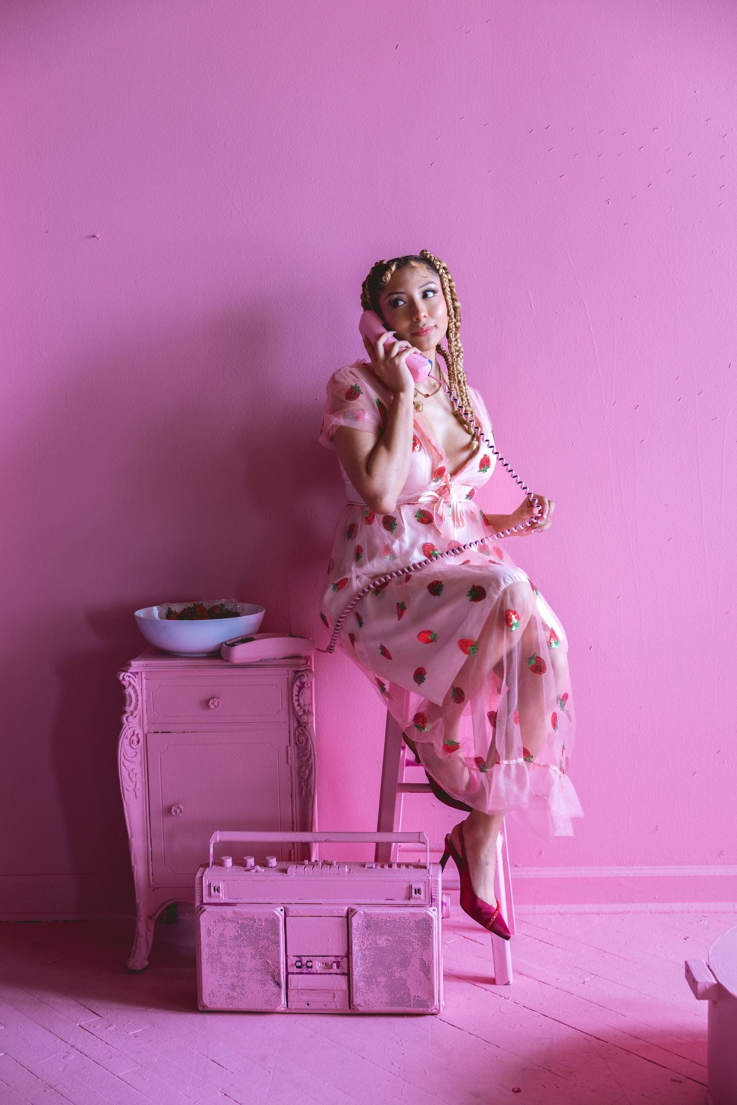 Woman in polka dot pink dress talks on retro phone beside pink boombox.