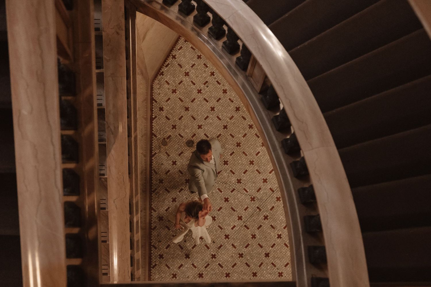 Aerial view of bride and groom walking through an ornate marble staircase in a grand building.