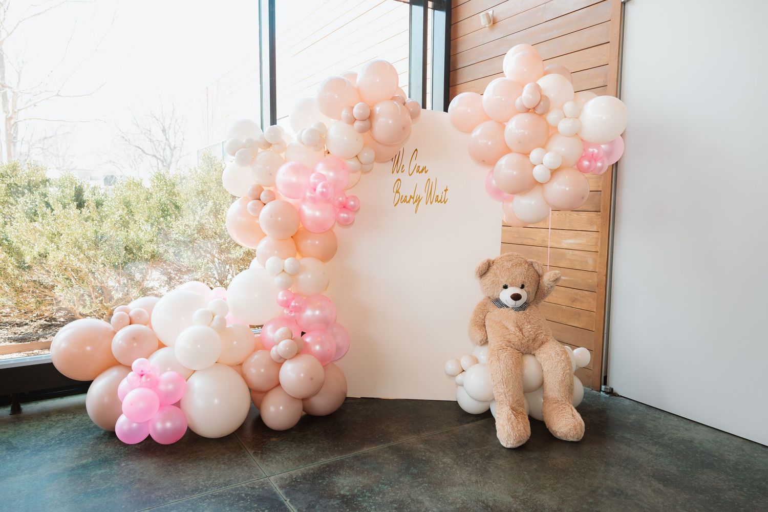 Pink and white balloon arch with teddy bear at a We Can Bearly Wait baby shower backdrop.