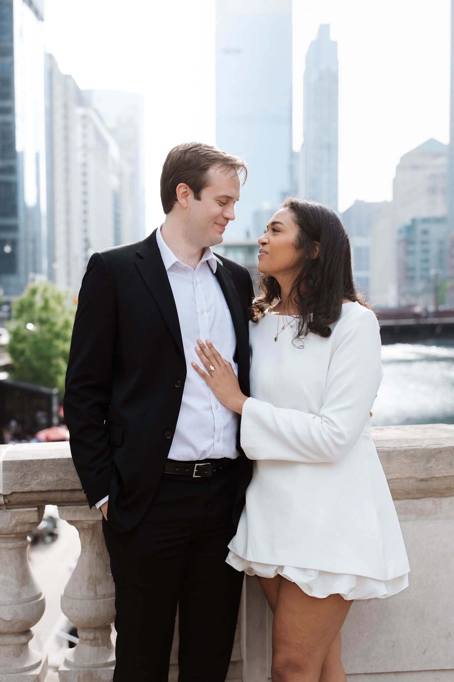 Couple in elegant black and white outfits sharing a tender moment on a bridge overlooking the Chicago skyline.