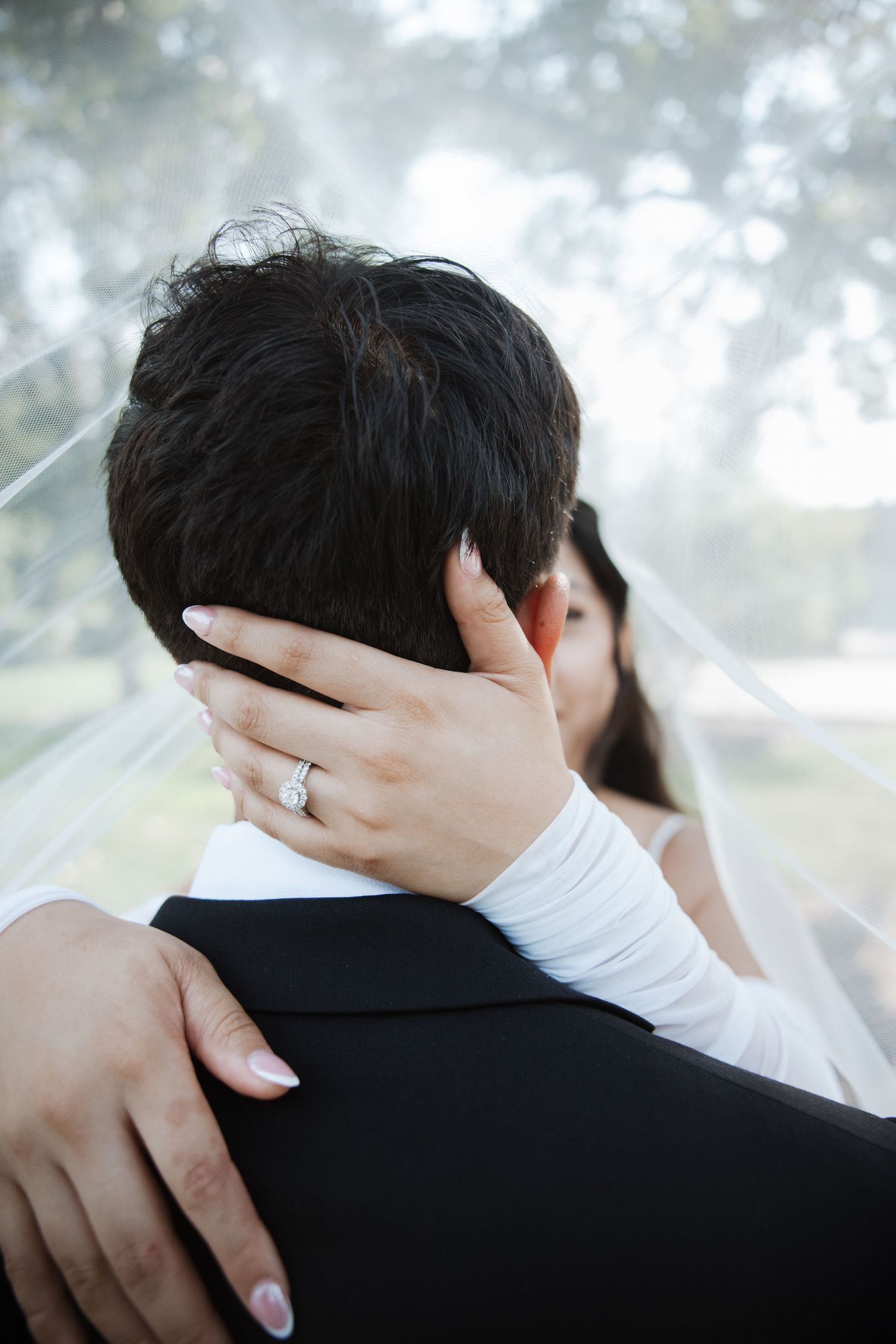 Bride's hand adorned with diamond ring tenderly cradling groom's head during wedding embrace.