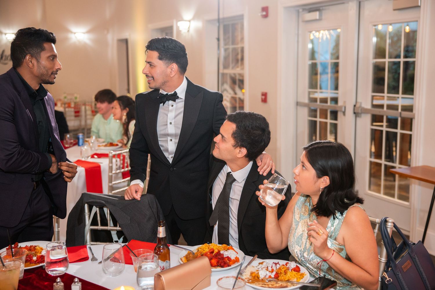 Guests in formal attire socializing and dining at an elegant indoor event with festive decor.