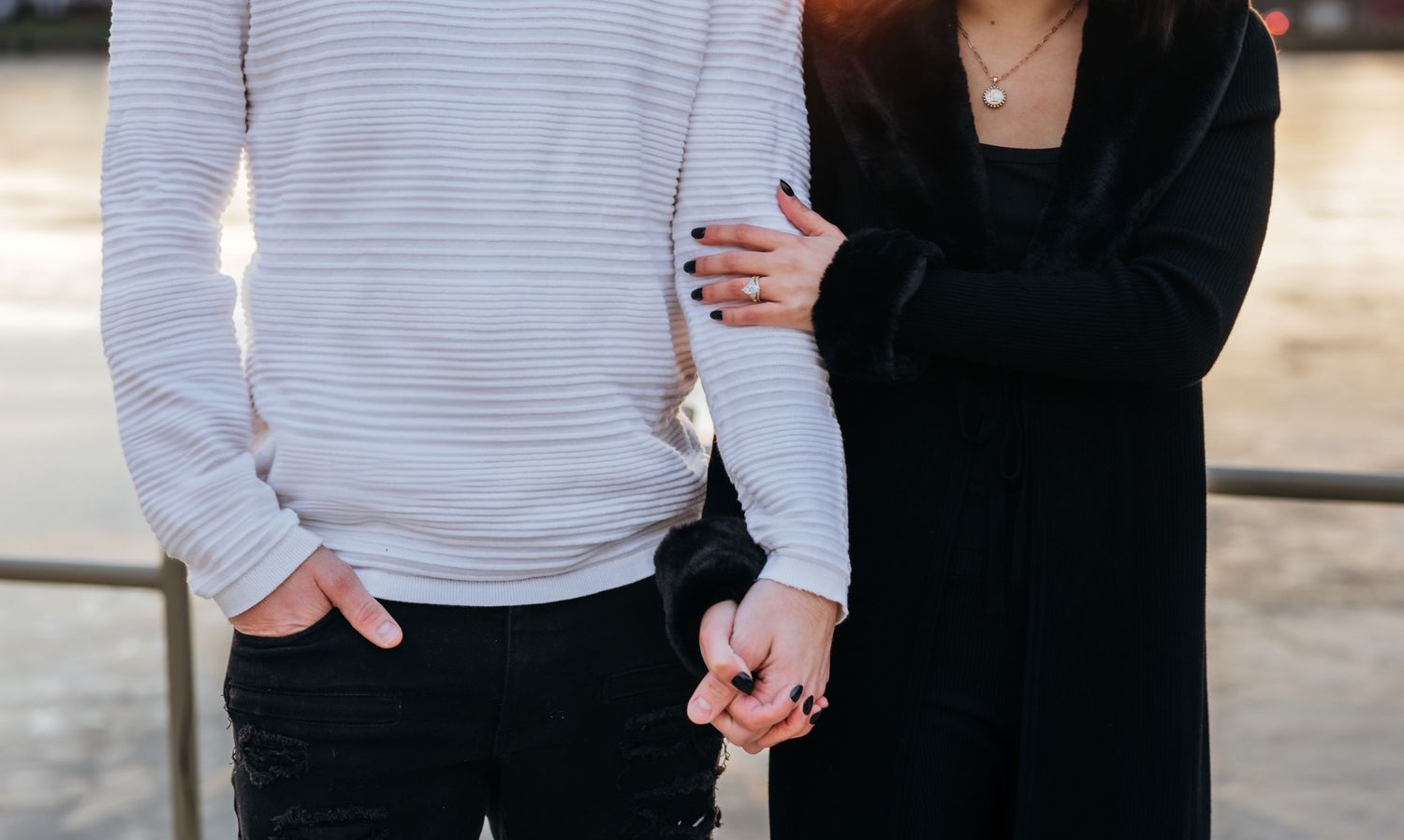 Close-up of a couple holding hands, woman wearing a diamond ring and black coat.
