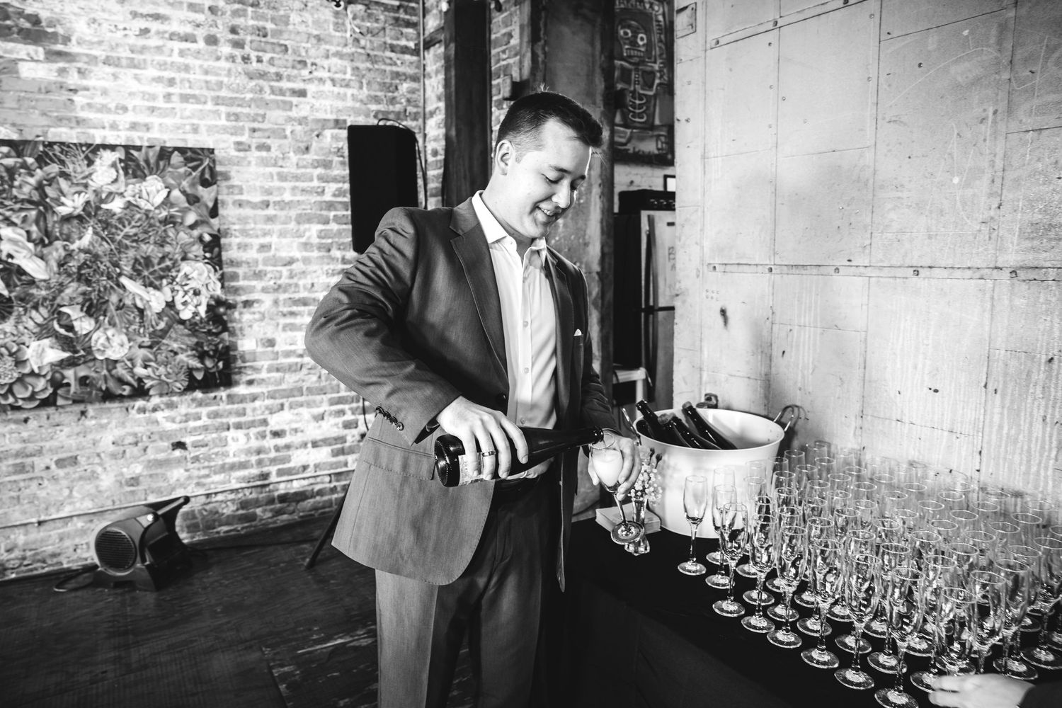 Black and white photo of a man in a suit pouring champagne at a reception bar.