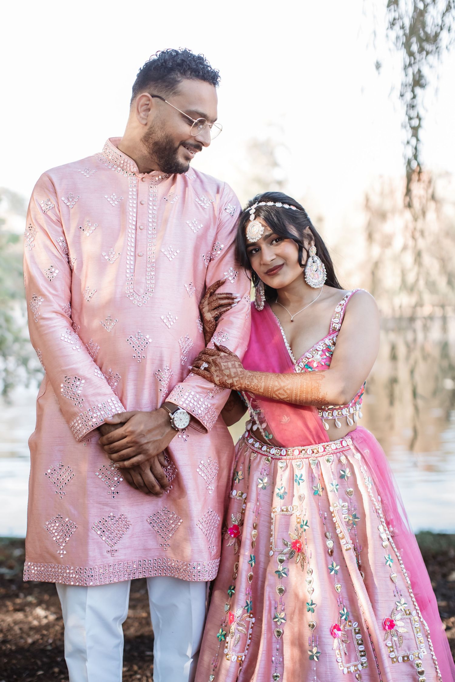 Indian couple in matching pink traditional wedding attire embracing outdoors.