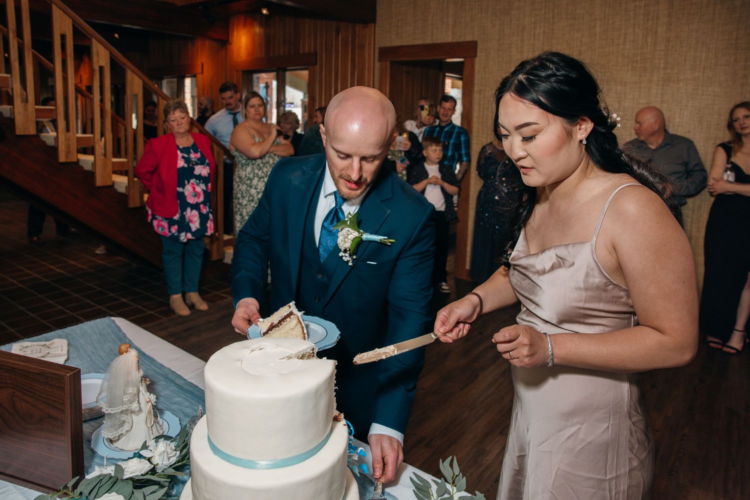Bride and groom cutting their three-tier white wedding cake together at their reception.