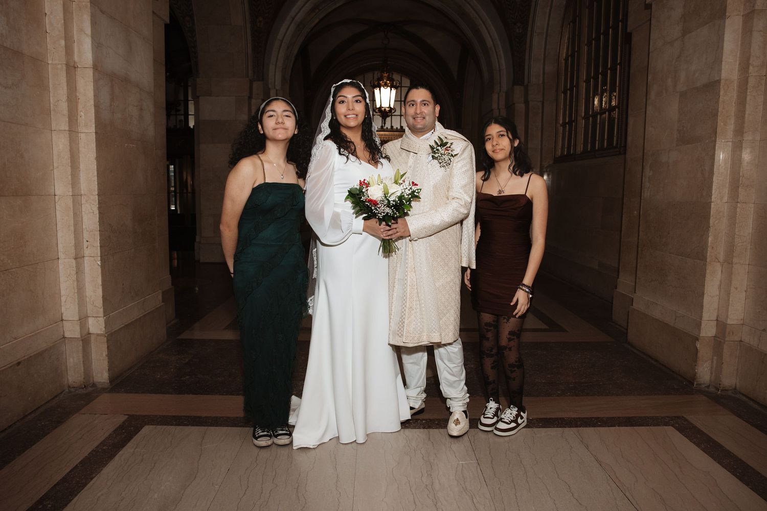 Bride and groom posing with two guests in an elegant stone hallway on their wedding day.