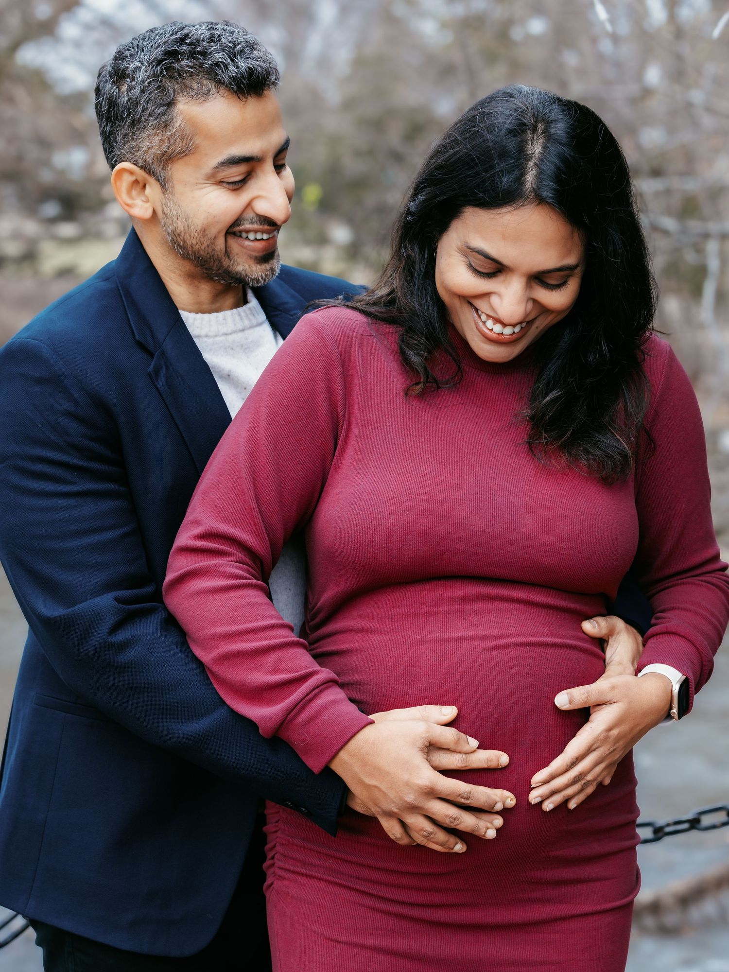 Joyful couple laughing together during outdoor maternity session, both holding baby bump.