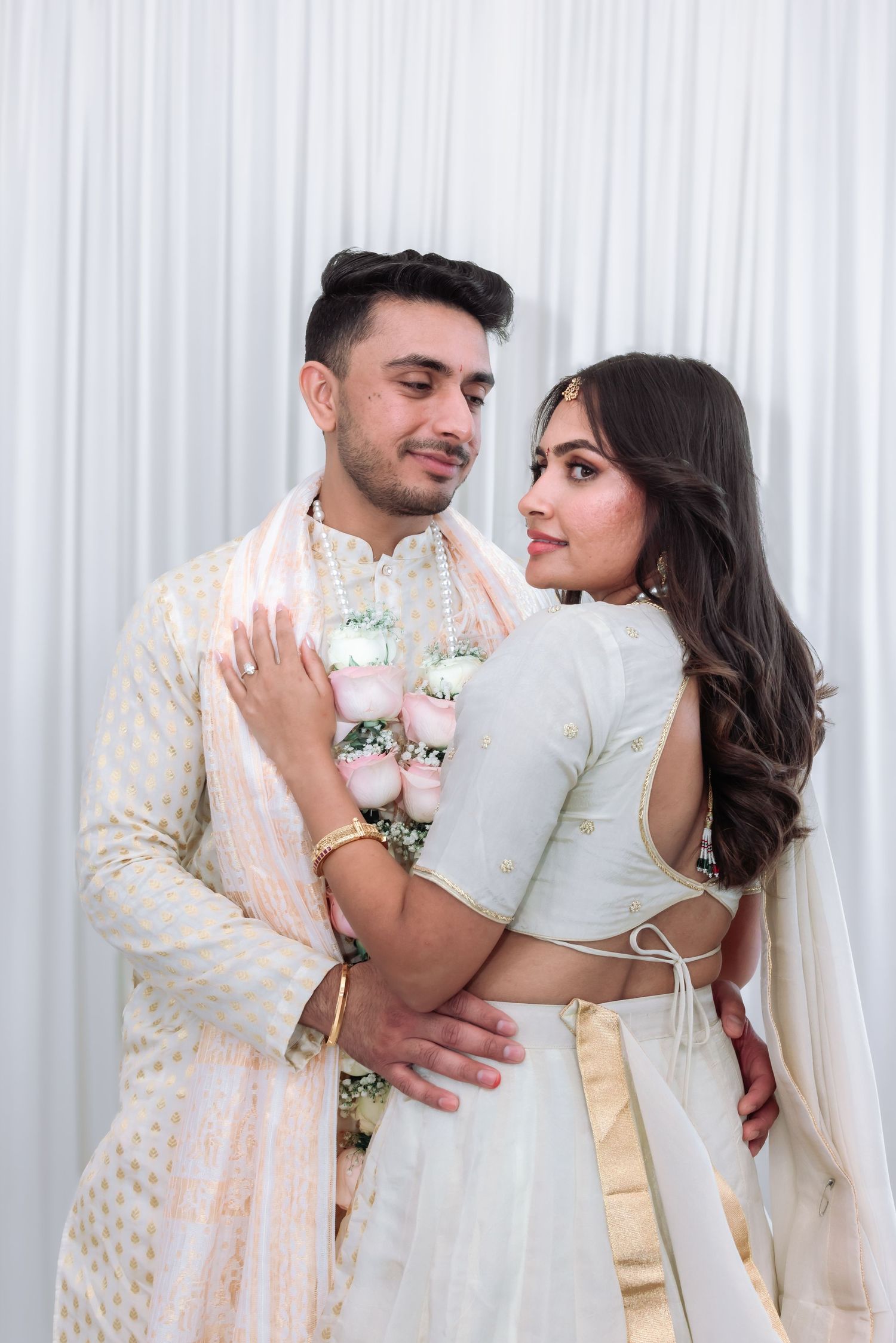 Indian couple embracing in matching white wedding outfits adorned with floral garlands during their wedding ceremony.