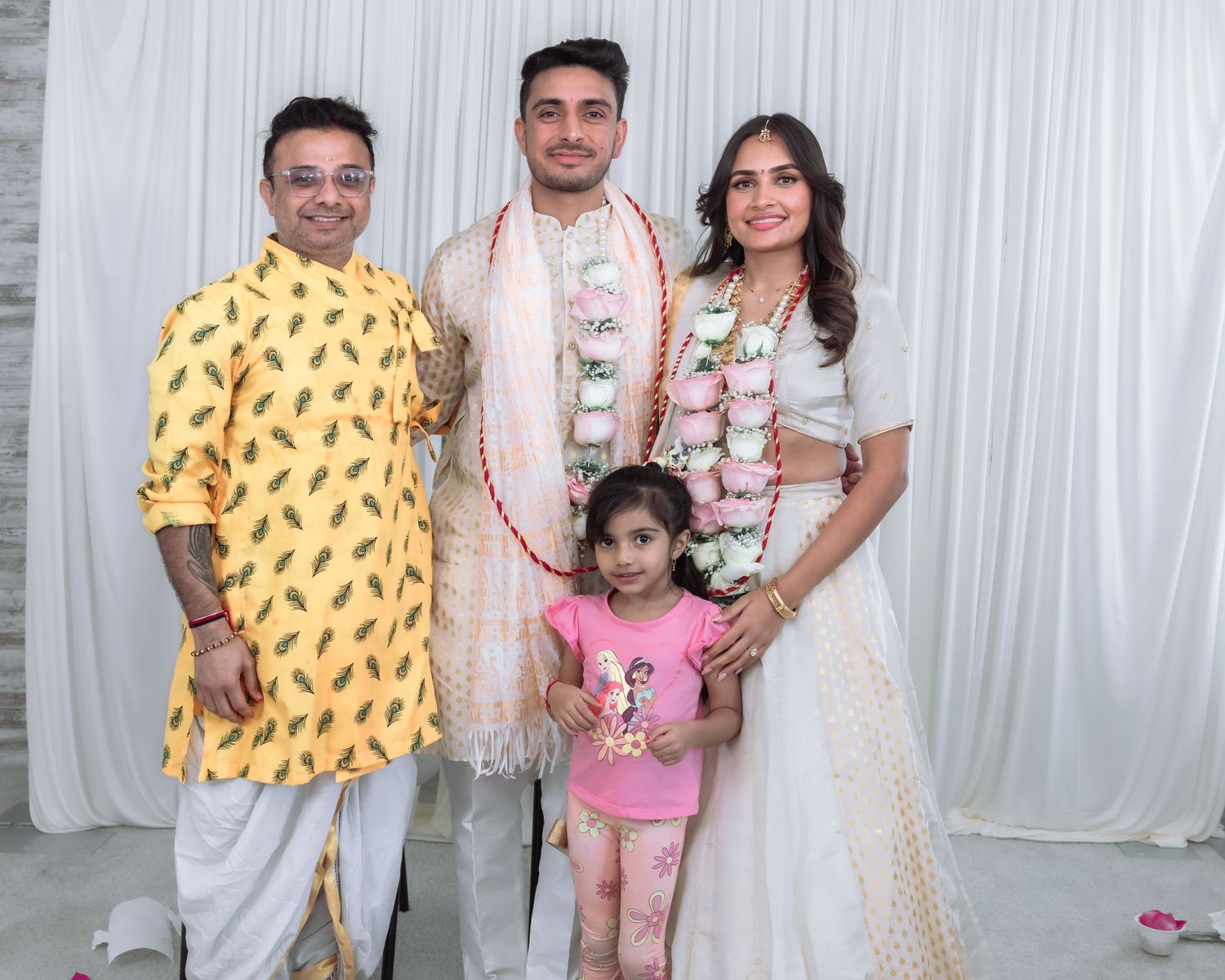 Man in yellow kurta and young girl pose with Indian bride and groom at wedding celebration.