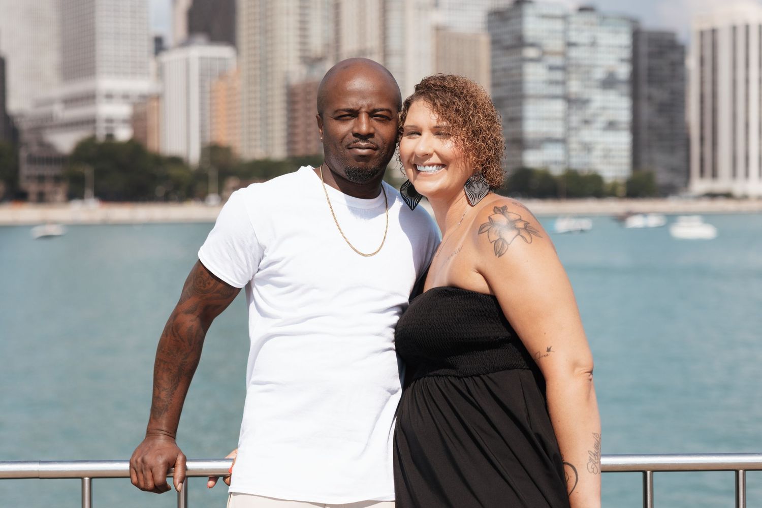 Interracial couple smiling together on Chicago waterfront with city skyline in background on sunny day.