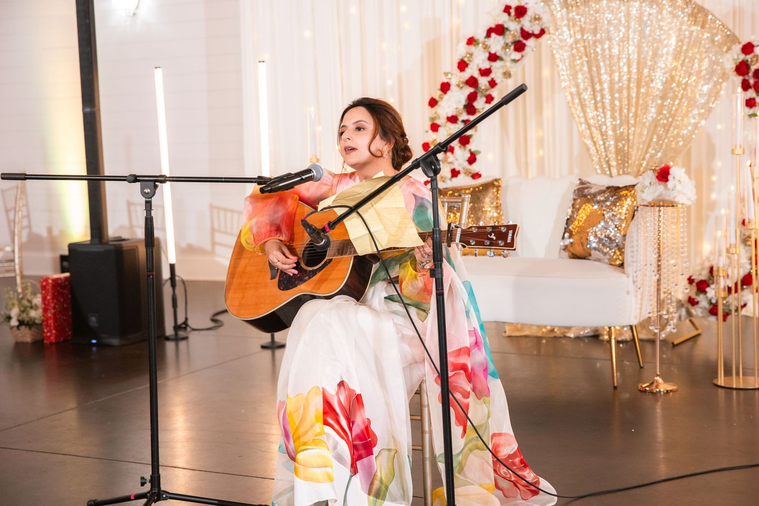 Woman in floral gown performing live acoustic guitar at wedding reception.