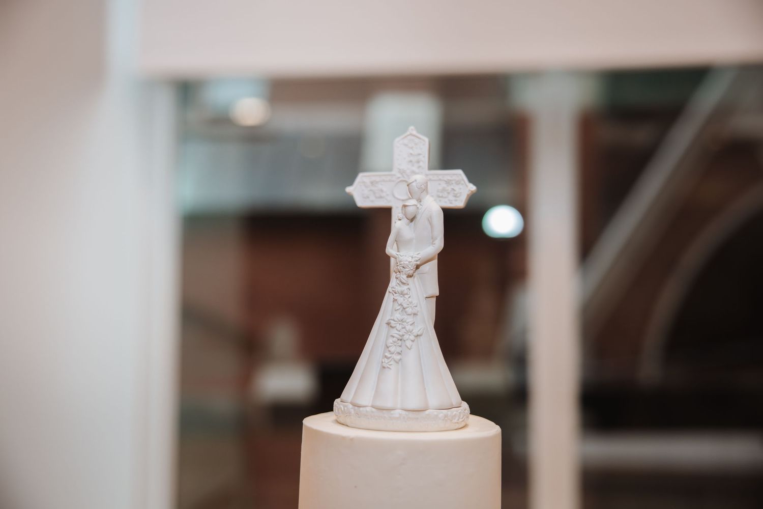 White ceramic wedding cake topper featuring bride, groom, and cross.