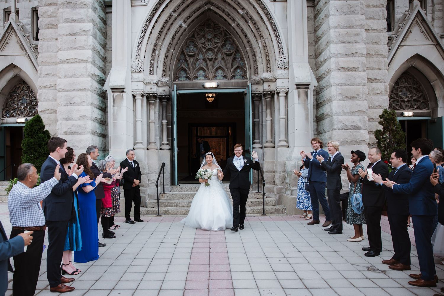 Newlyweds exit Gothic church entrance as guests applaud and celebrate their wedding ceremony.