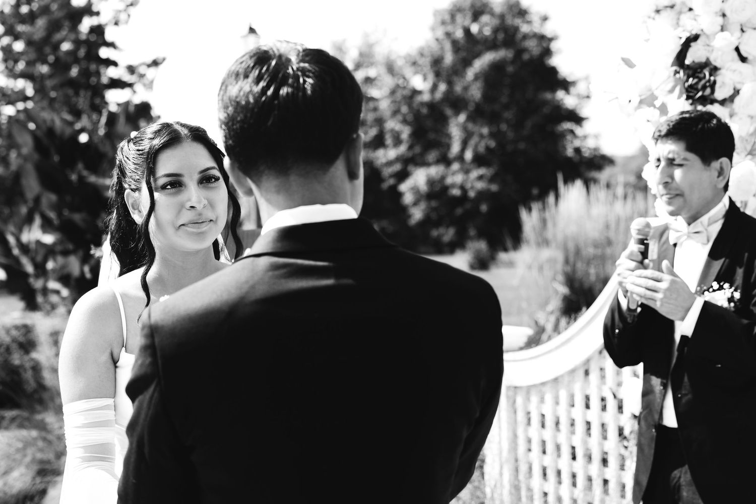 Black and white photo of bride gazing at groom during intimate outdoor wedding ceremony.