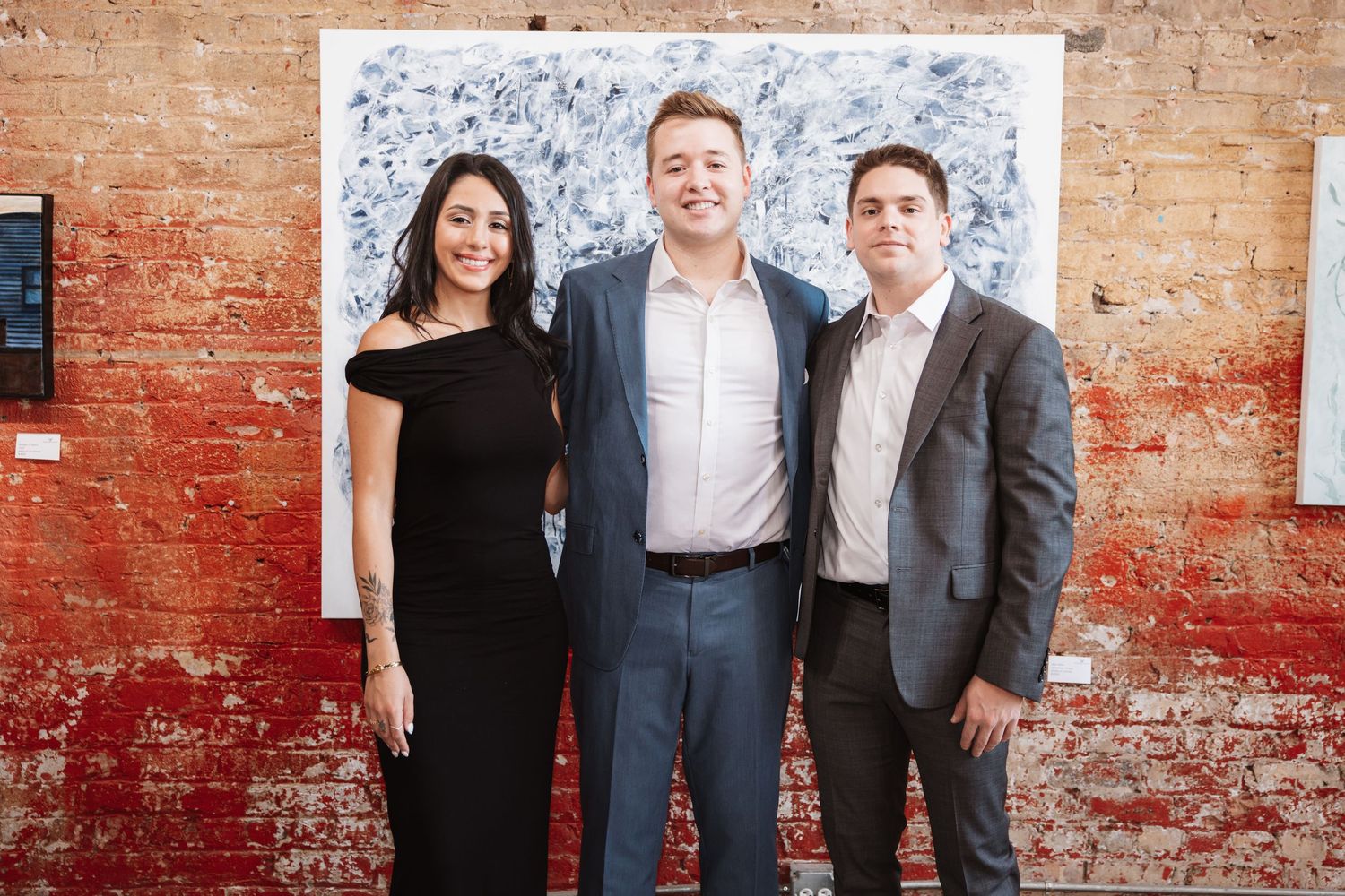 Three professionals posing together in front of abstract artwork at an art gallery event.