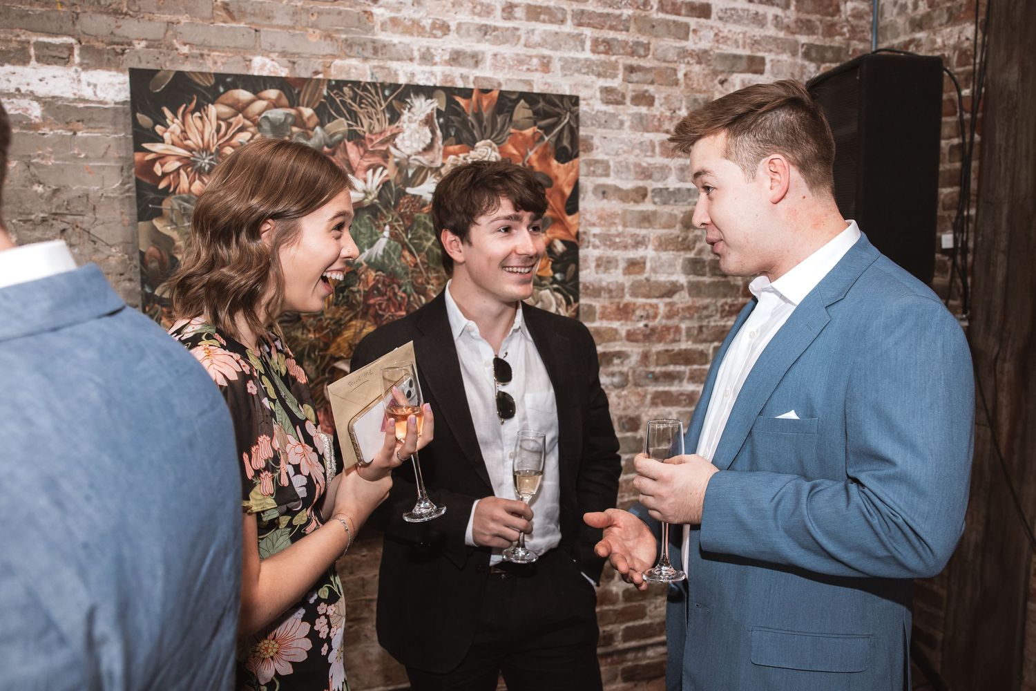 Three guests laughing and holding champagne at an art gallery social event.