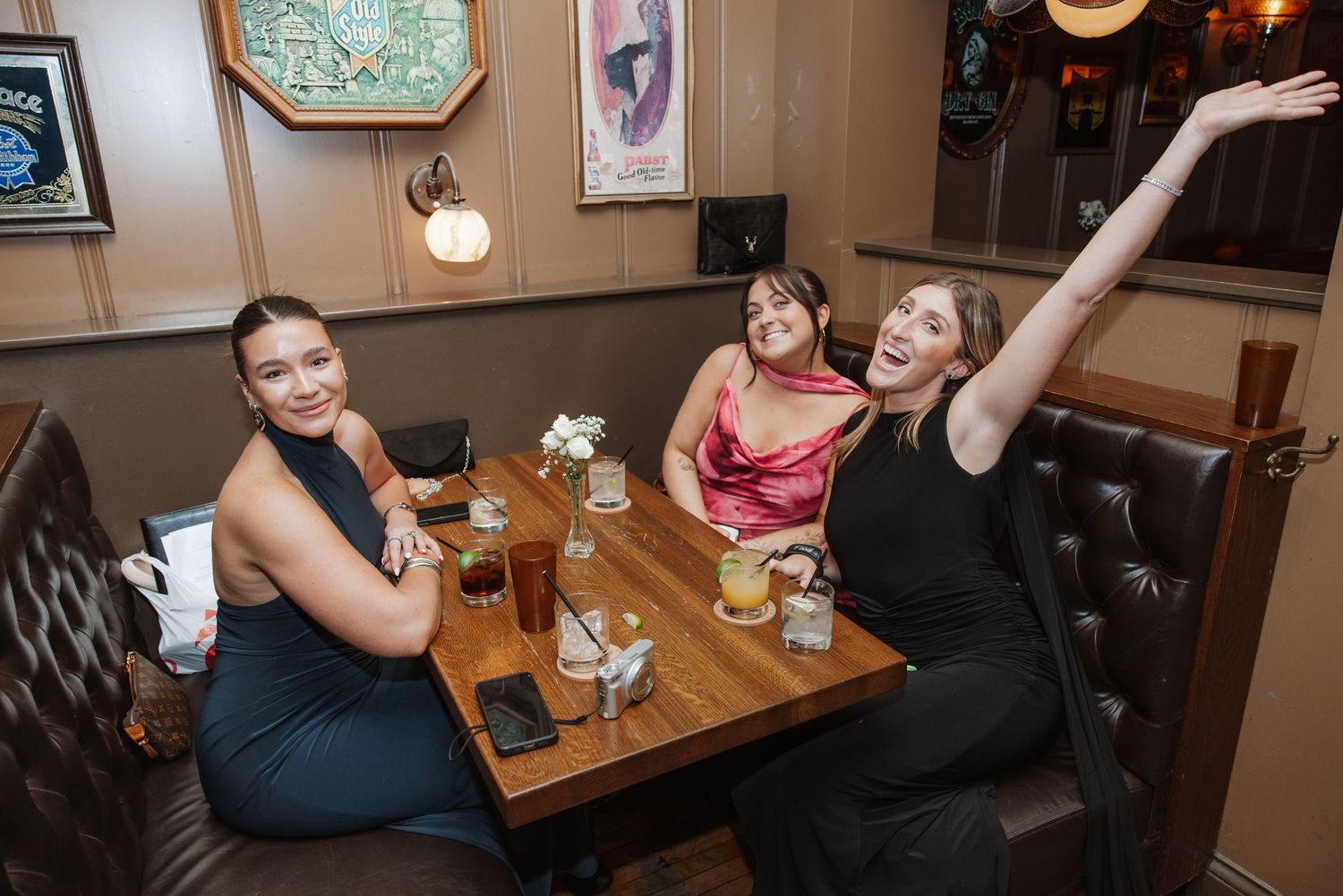 Three women smiling and celebrating at a table in a restaurant during a wedding reception.