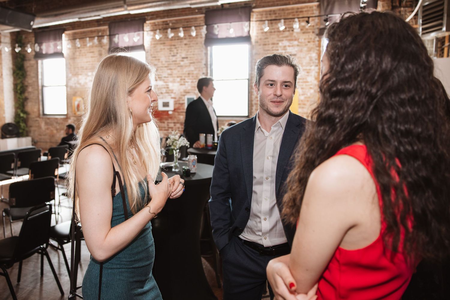 Three guests in formal attire having a conversation in a rustic brick-walled venue.