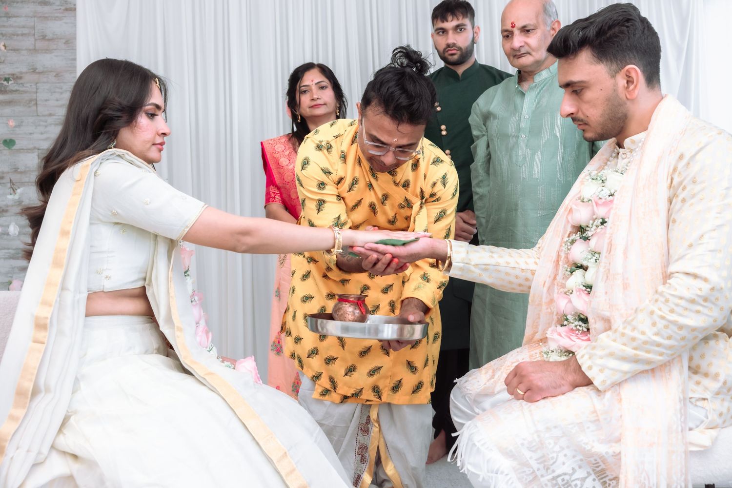 Indian wedding guests performing traditional hand ceremony with bride and groom in elegant ethnic attire.