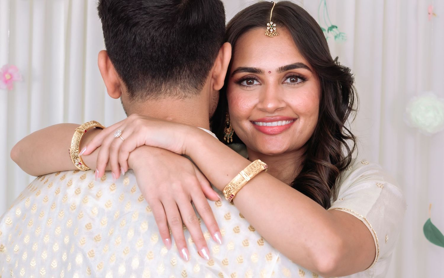 Smiling Indian bride in white lehenga embraces groom during traditional wedding celebration.