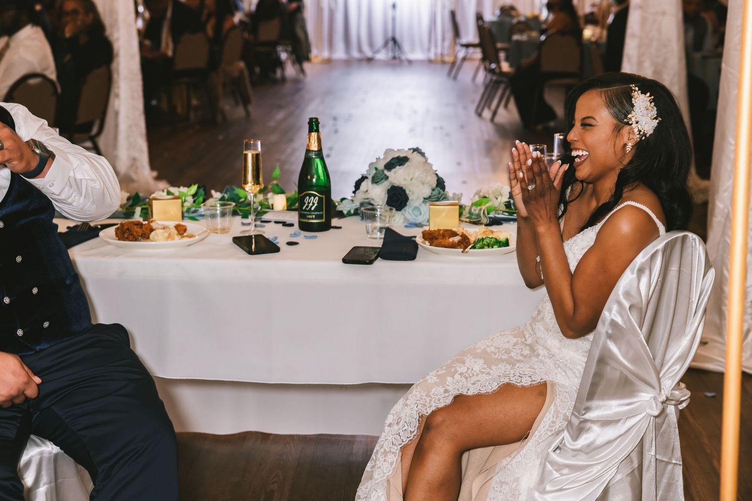 Bride in white gown smiling and clapping at her wedding reception table.