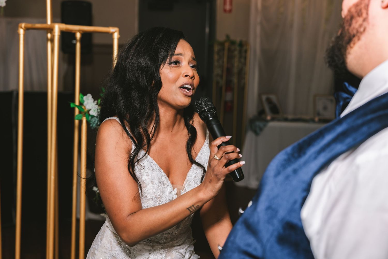 Bride in lace wedding gown singing into microphone during wedding reception first dance.