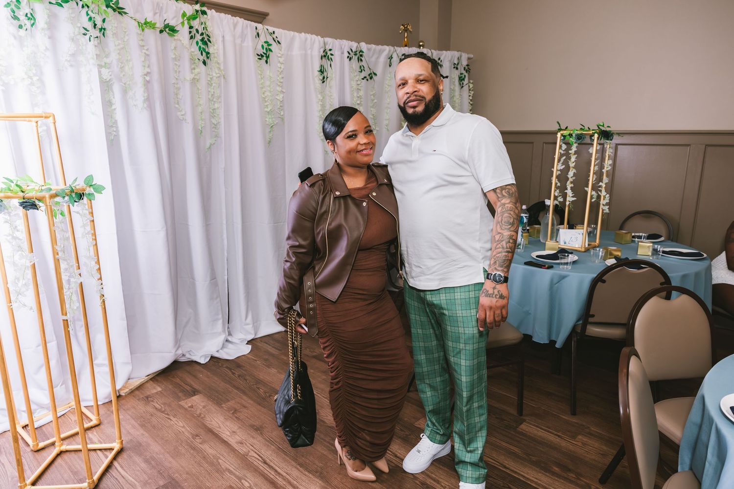 Couple posing together at a wedding reception in front of a white draped backdrop with greenery.