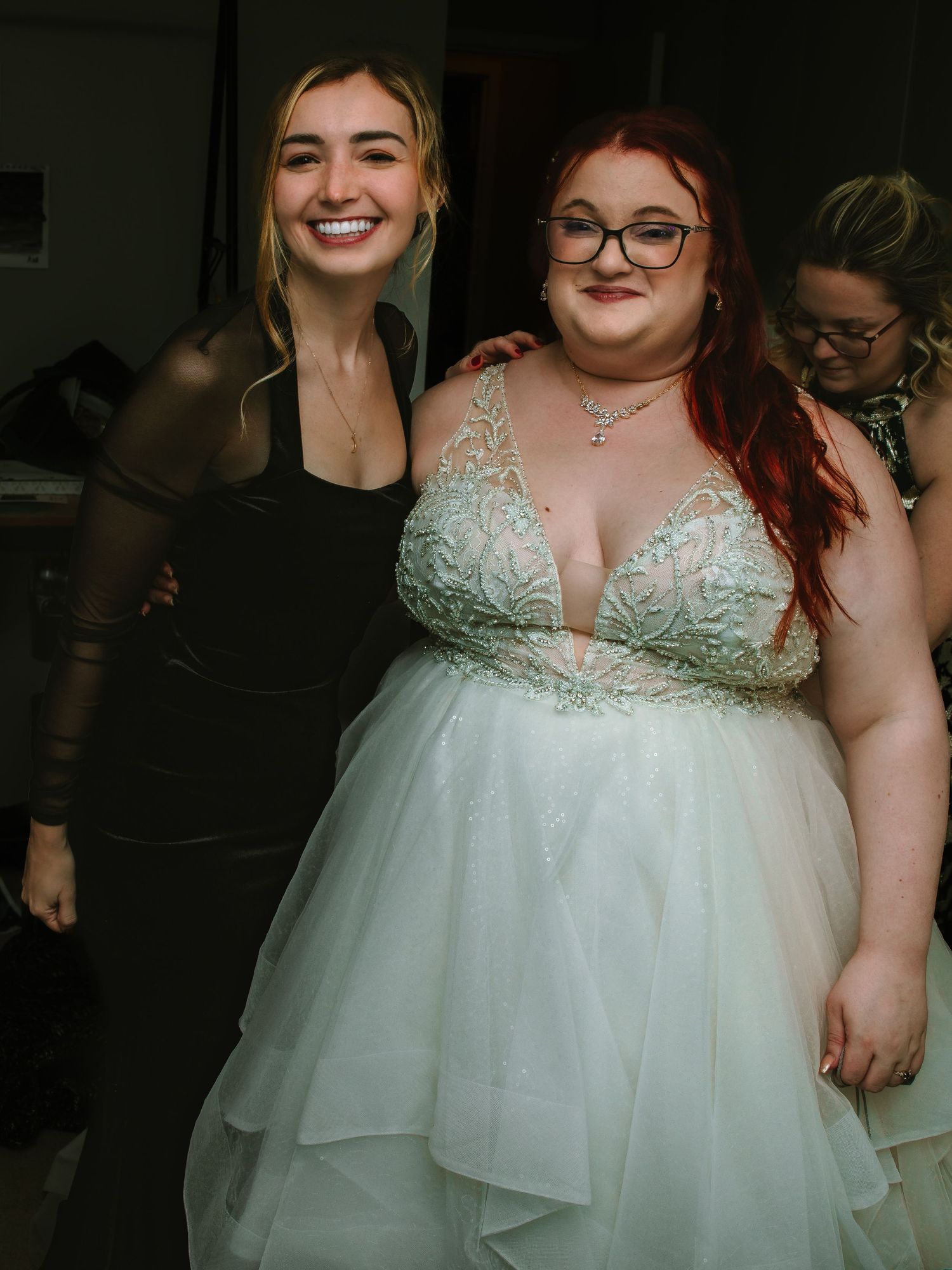 Bride in white beaded wedding gown posing with a smiling woman in a black dress.