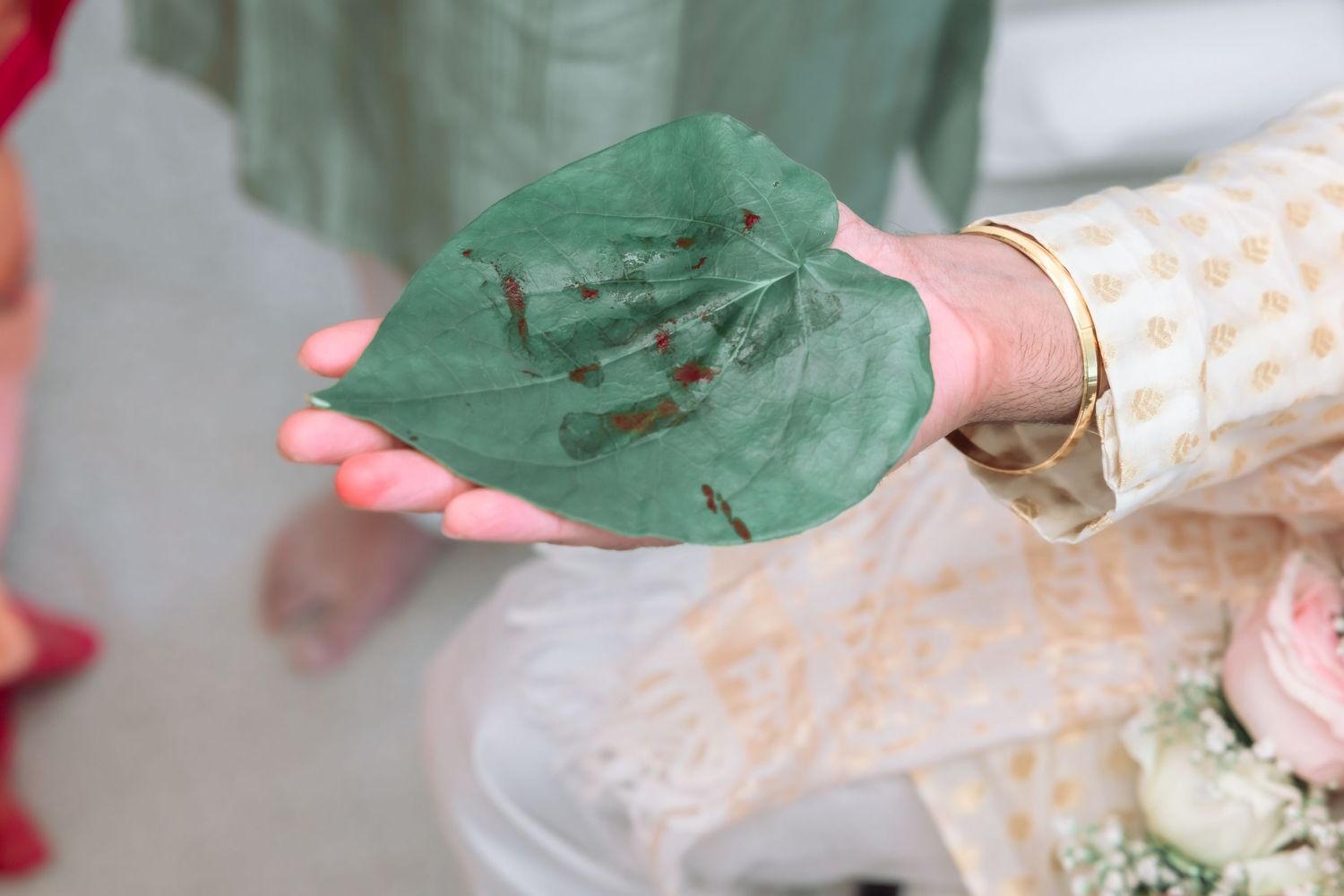 Close-up of a green betel leaf with henna imprints held during a traditional South Asian wedding ritual.