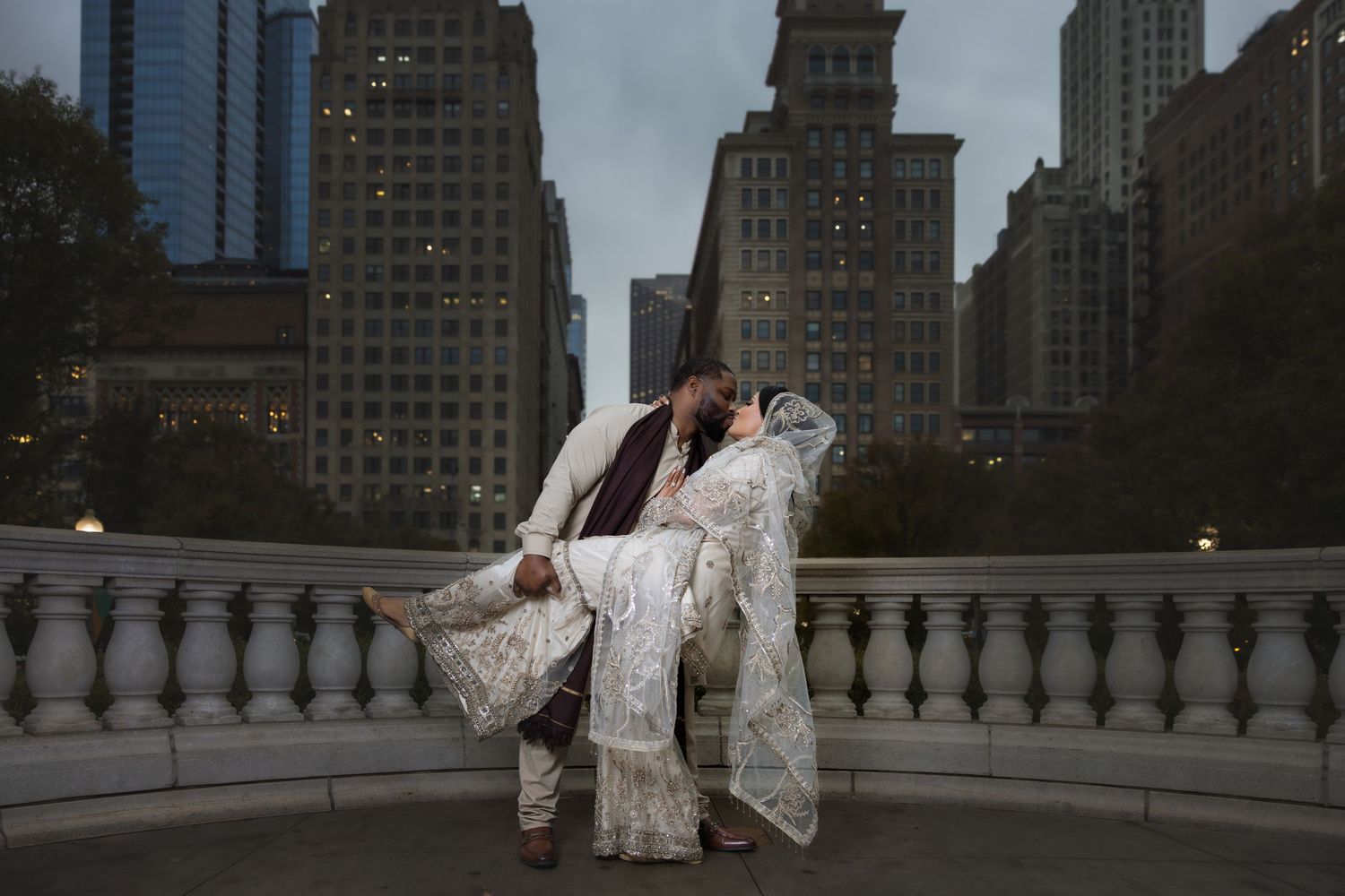 Groom dips bride in white lace wedding outfit for romantic kiss against Chicago city skyline.