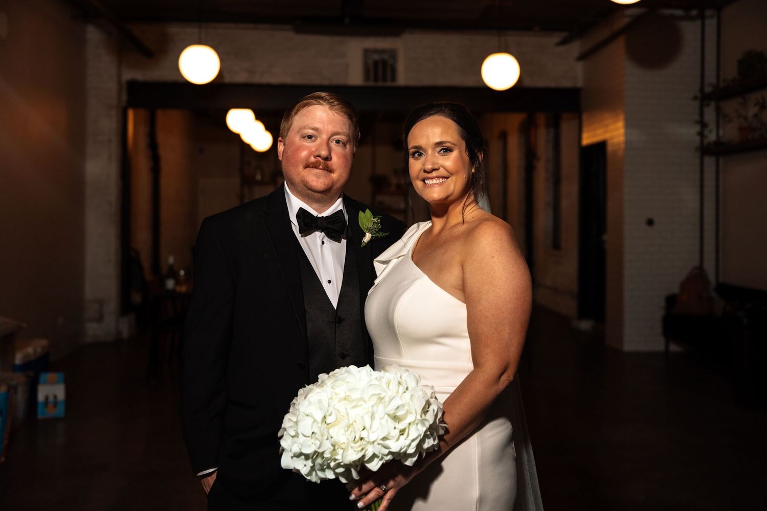 Bride and groom smile together at wedding reception, bride holding white hydrangea bouquet.