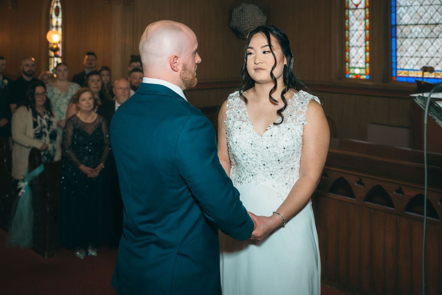 Bride smiling at groom while holding hands during wedding ceremony in a historic church.