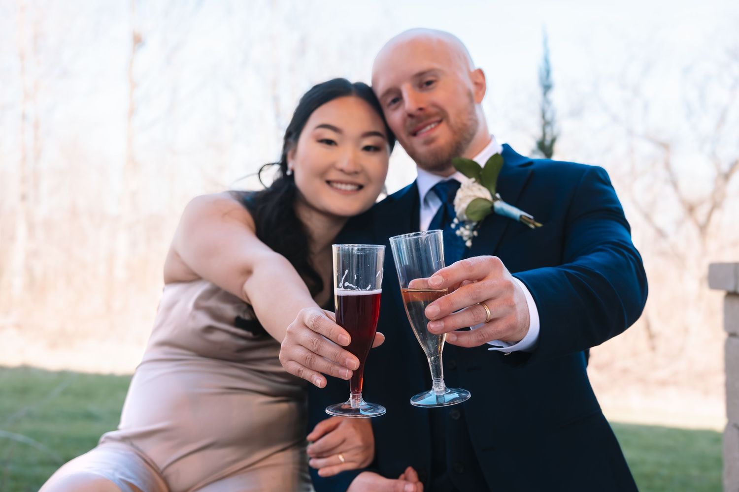 Bride and groom cheerfully toasting with red wine glasses at outdoor wedding.