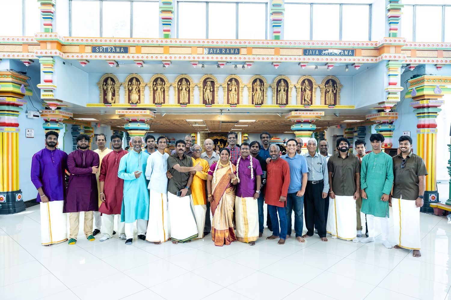 Large group of men in traditional South Indian attire posing outside a decorated Hindu temple.