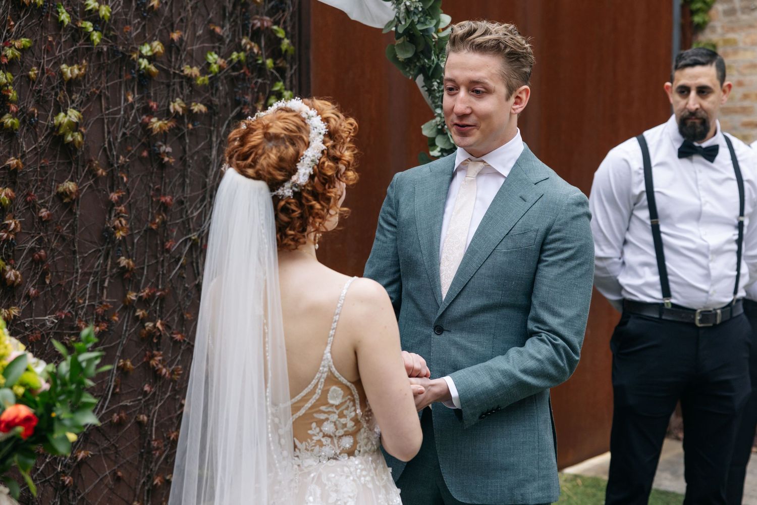 Groom smiles at red-haired bride during intimate outdoor wedding ceremony with groomsmen standing behind.