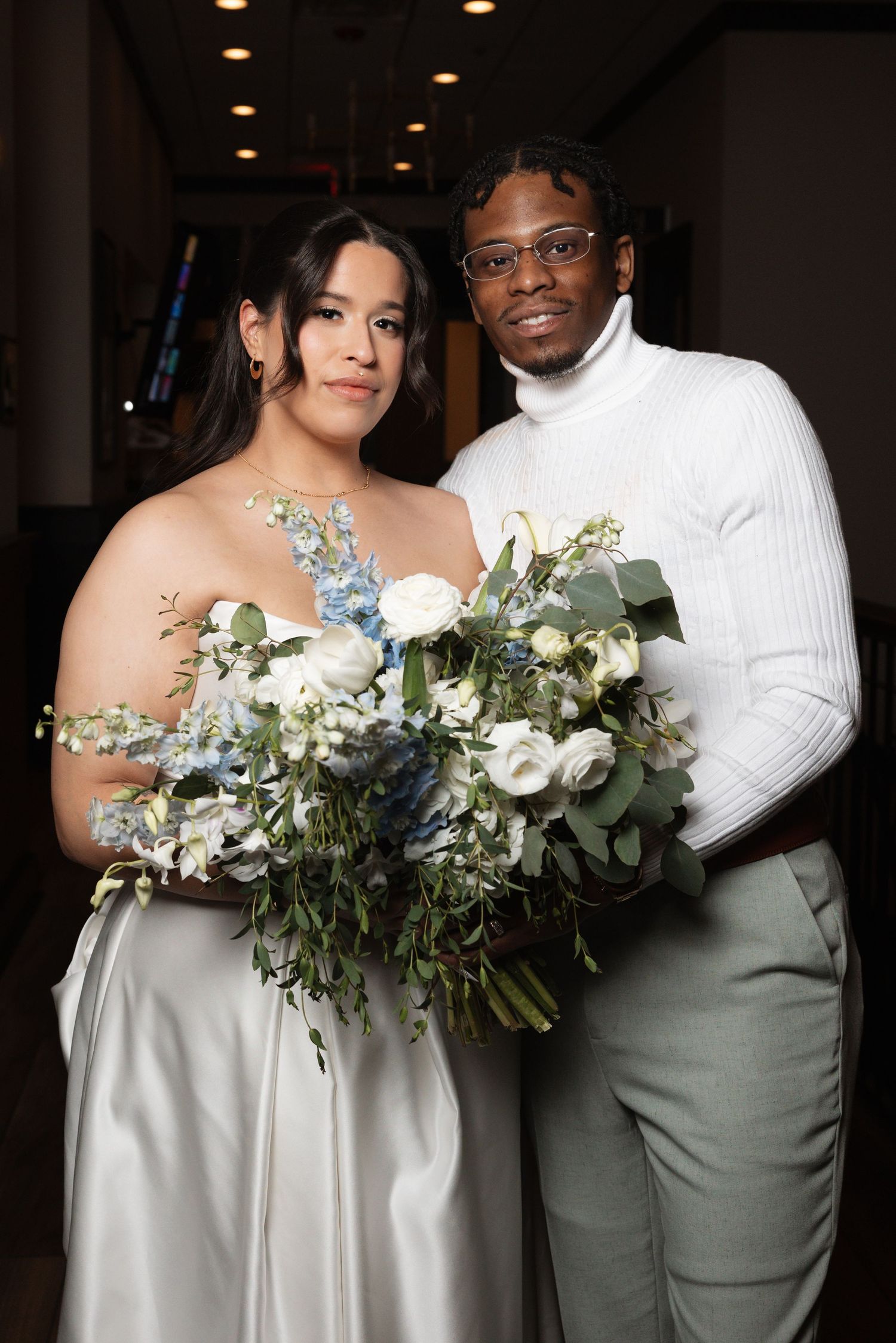 Bride and groom posing with large blue and white floral bouquet at reception.