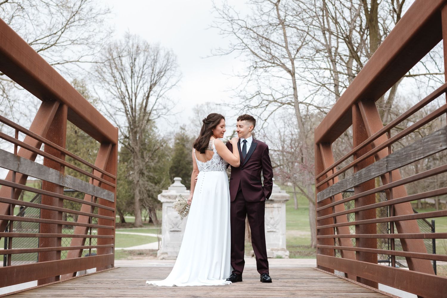 Bride and groom share a romantic moment on a wooden bridge surrounded by trees.