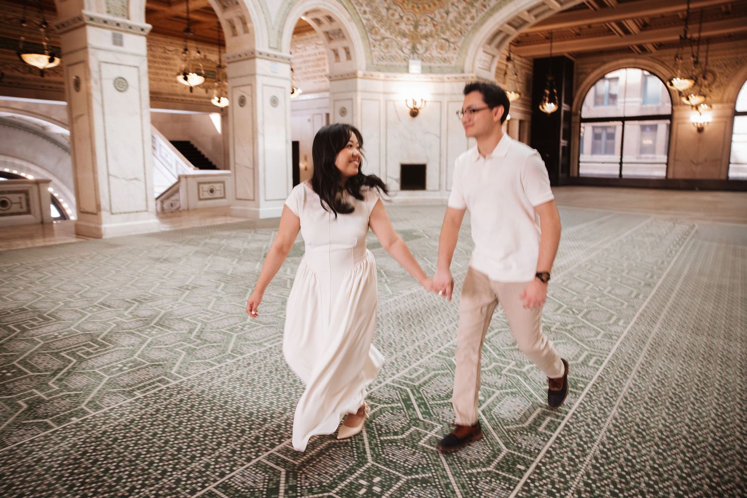Smiling couple walks hand in hand across elegant patterned ballroom floor.