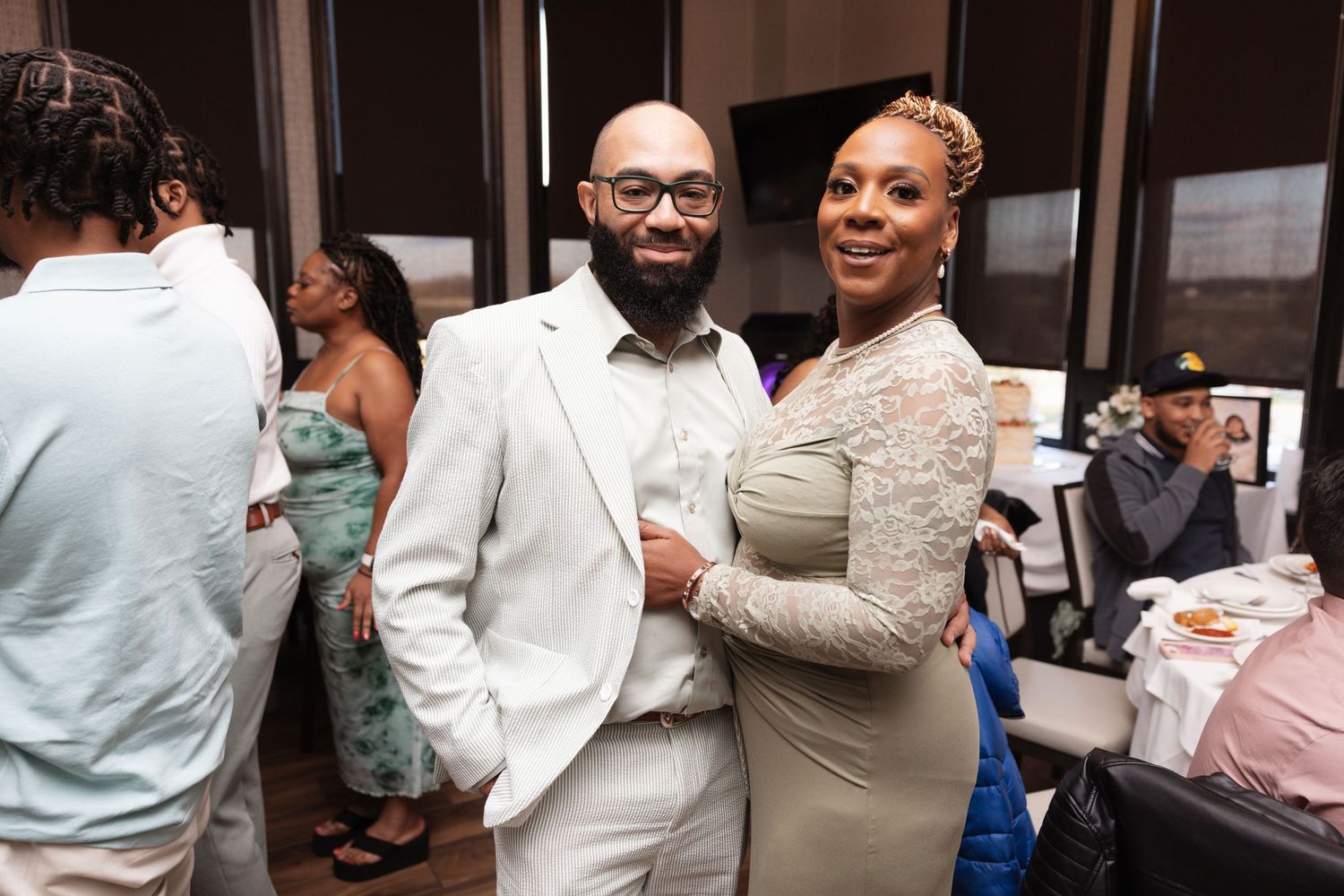Couple posing together at wedding reception, man in white suit and woman in gray dress.