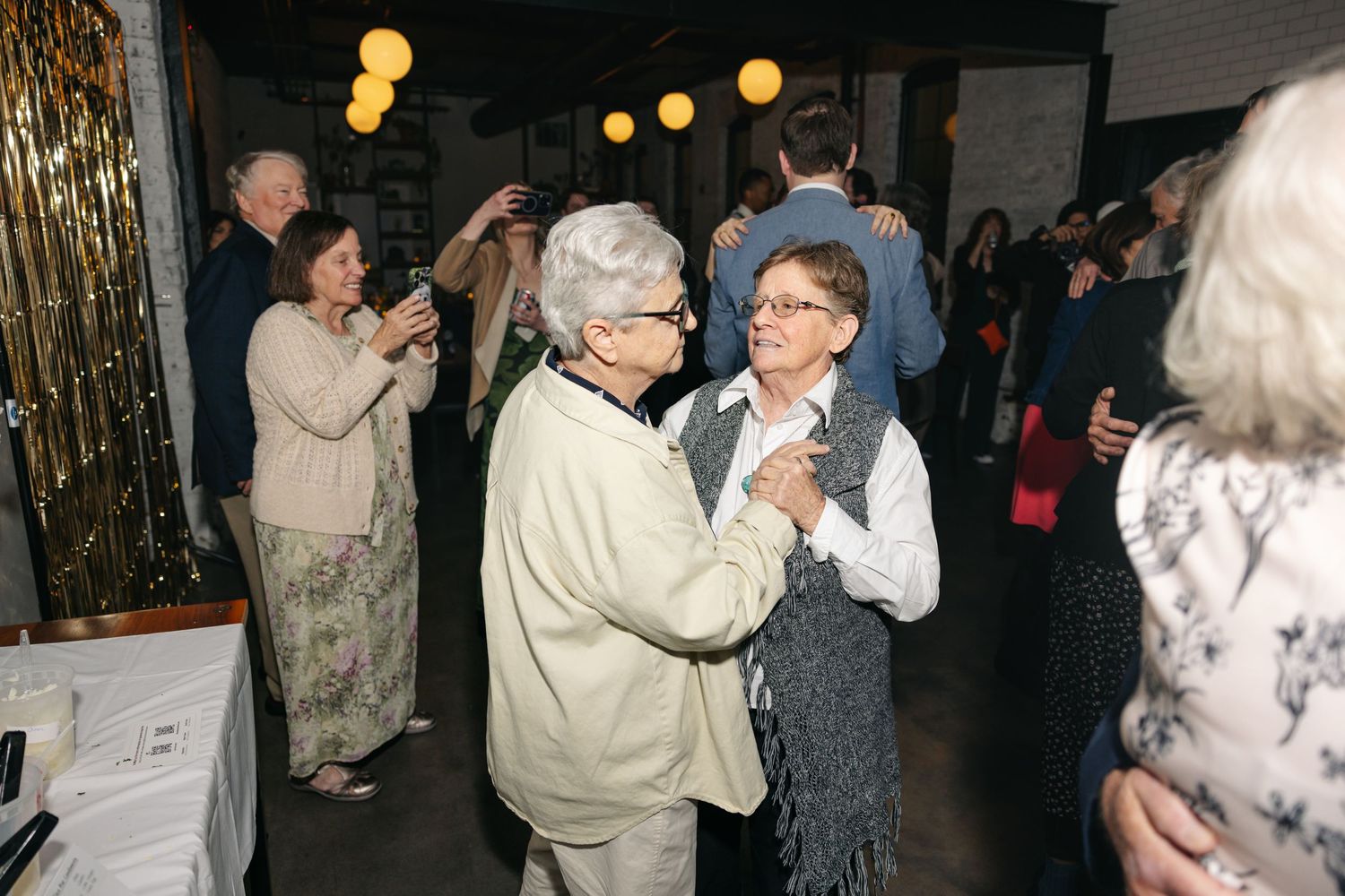 Two elderly women share a slow dance together on the dance floor at a warm wedding reception celebration.