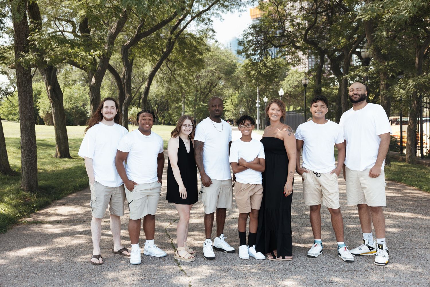 Family group of eight posing outdoors in a park wearing coordinated white and beige outfits.