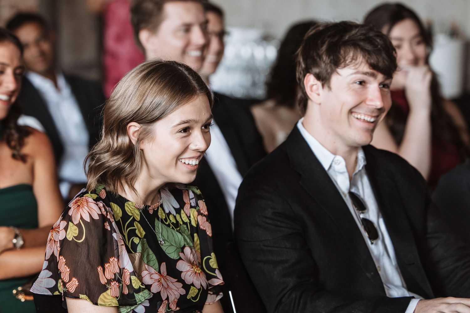 Happy couple laughing together while seated as guests at an elegant wedding ceremony.