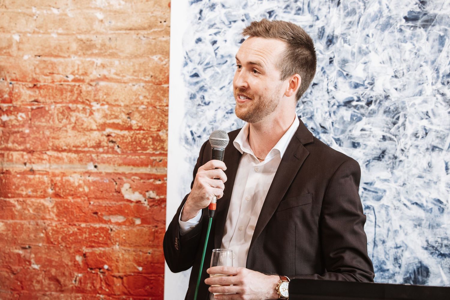 Smiling man in blazer speaks into microphone at podium during an elegant indoor event.