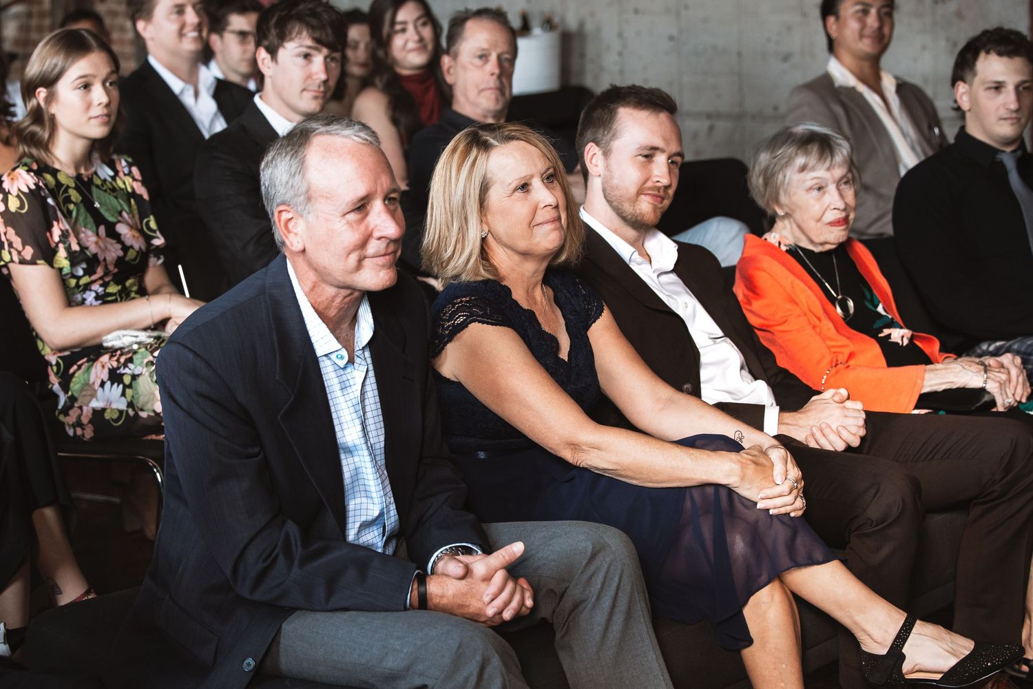 Family members seated together as wedding ceremony guests in a warmly lit venue.