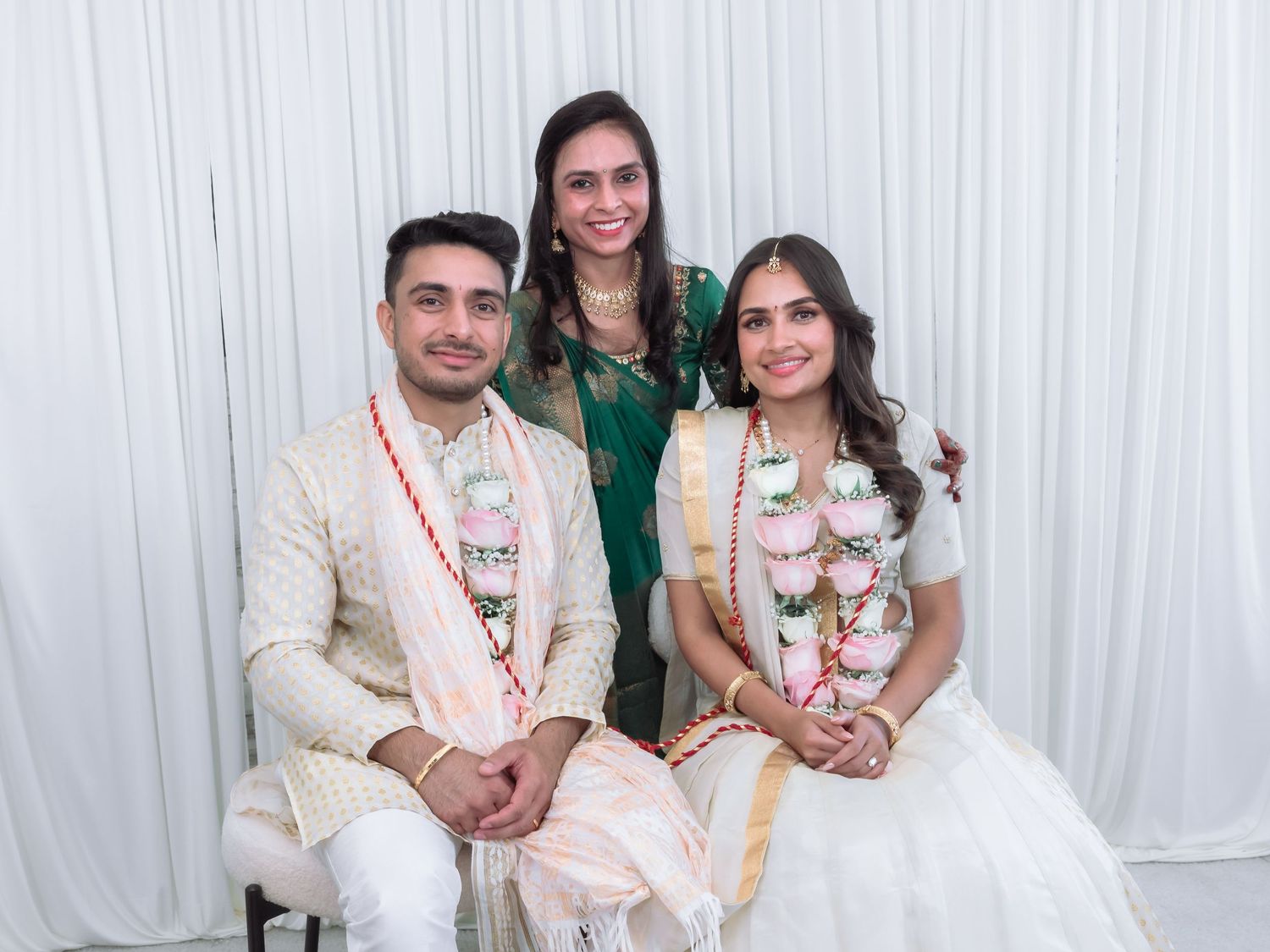 Indian wedding couple in garlands seated with woman in green saree for formal portrait.
